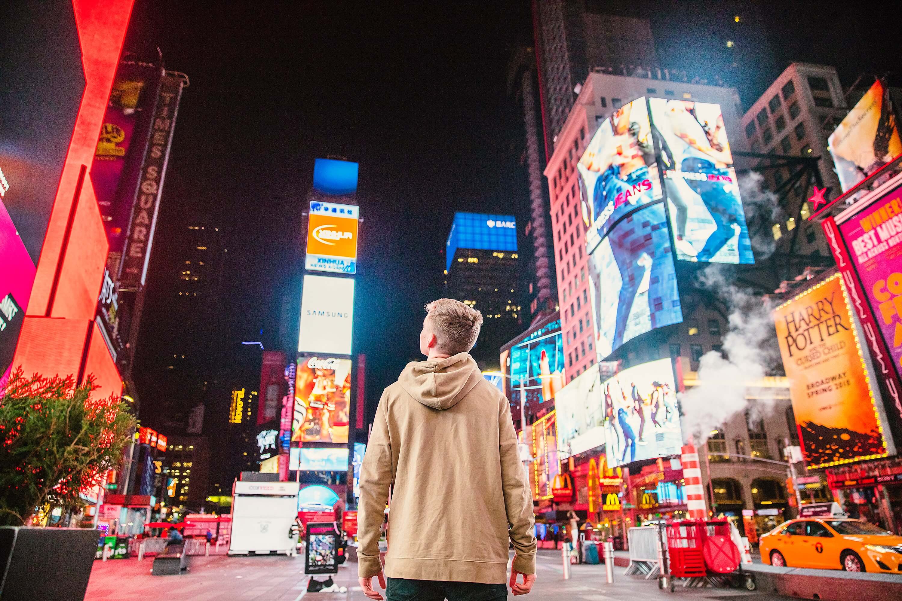 Young man standing in Times Square looking at billboards